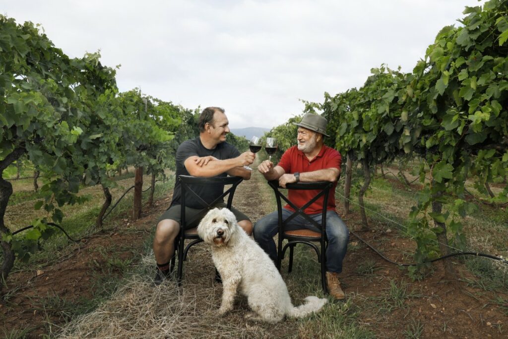 Hunter Valley Winemaker Mike De Iuliis and his Dad Joss De iuliis celebrate in a vineyard with the groodle Lucy